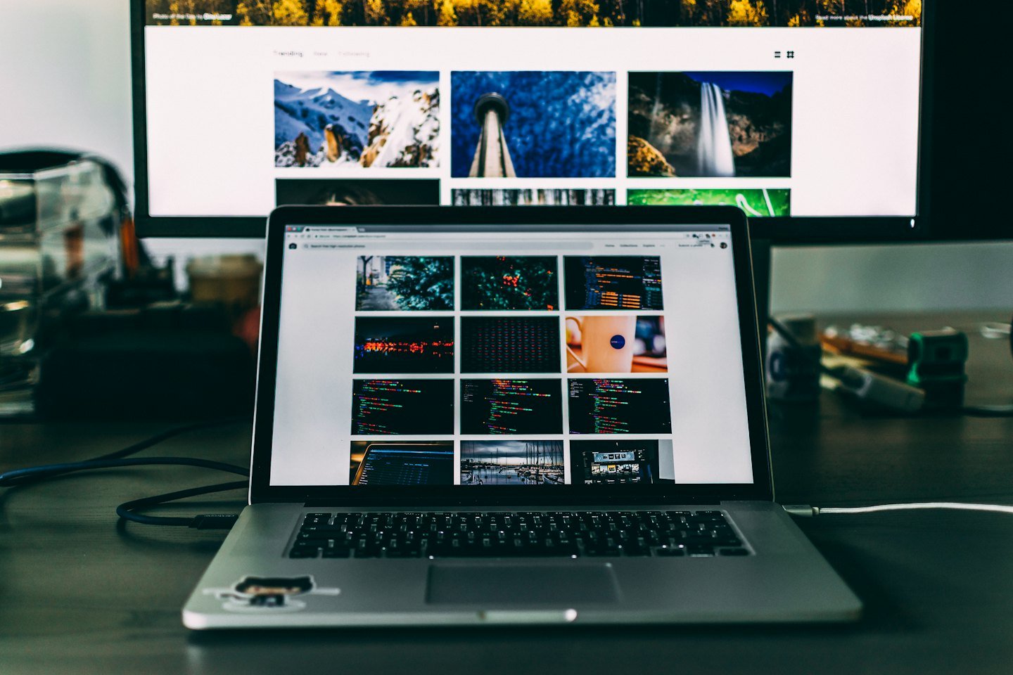 A laptop and desktop monitor display active websites on a desk.
