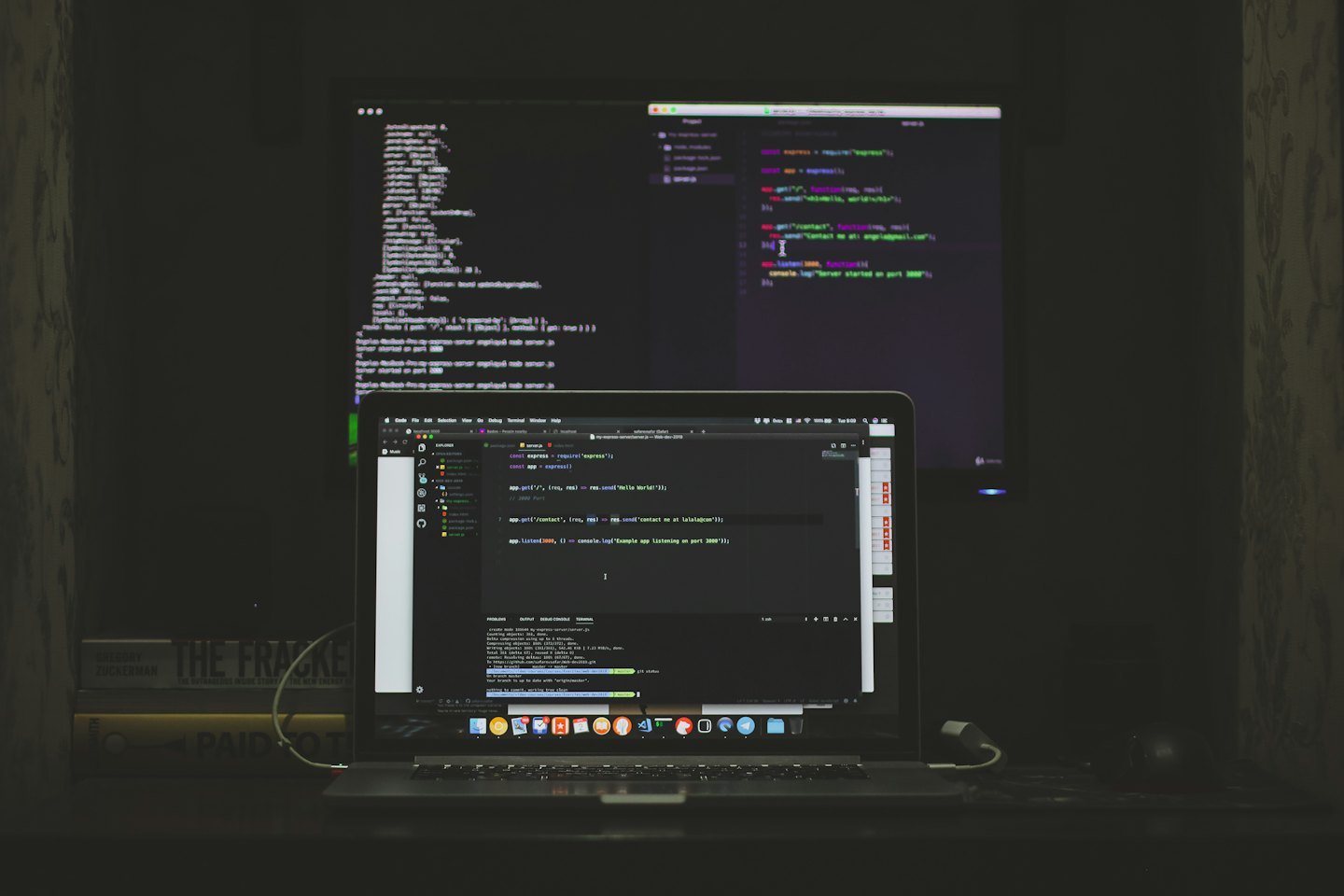 Laptop and external monitor displaying code on a desk.